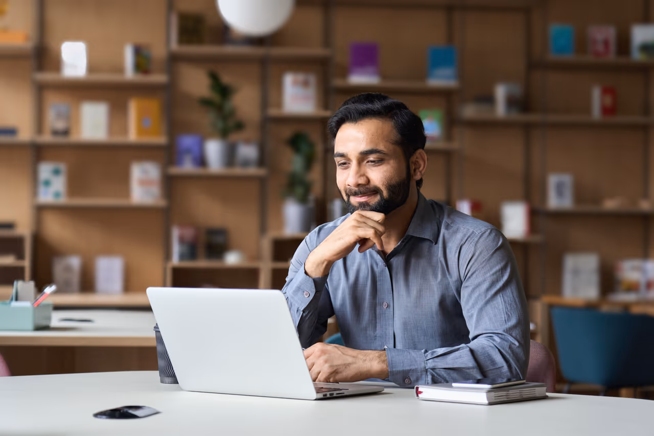 Smiling,Indian,Businessman,Working,On,Laptop,In,Modern,Office,Lobby